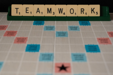 A scrabble board with the word 'teamwork' behind it in scrabble tiles