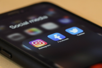 A mobile phone lies flat on a table - on screen are the instagram, Facebook and twitter icons under the folder title social media